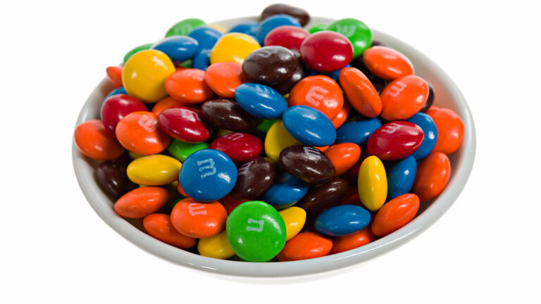 a bowl full of colorful M&M's on a white background