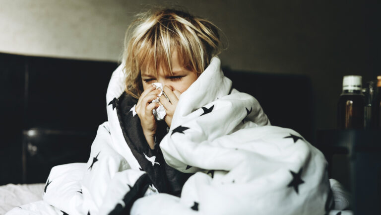 A cold today helps keep the COVID away A blond child wrapped in a duvet blows their nose