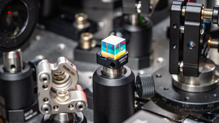 Lasers can eavesdrop on microbes, including viruses a photo of a laser beam splitter, a small colorful cube, surrounded by laser equipment
