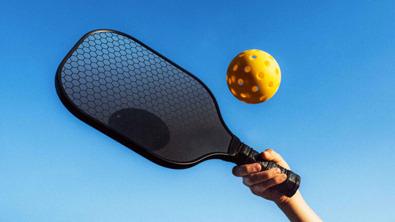 To reduce drag on vehicles, researchers turned to pickleballs a photo of a hand holding a pickleball paddle about to hit a yellow pickleball