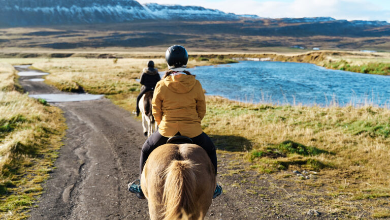 Horses became gentle and easy to ride thanks to two gene mutations Two people riding horses by an alpine pond are shown from behind.