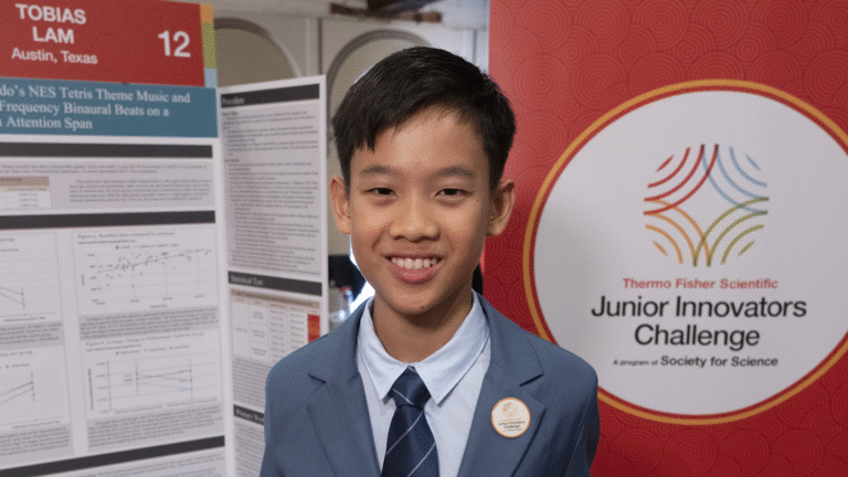 Listening to slightly different sounds in each ear may boost focus, teen finds Toby Lam stands in front of a red background and his poster about how sound can affect people's focus during a task.